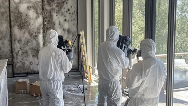 Crew in protective suits setting up equipment to assess mold in a room